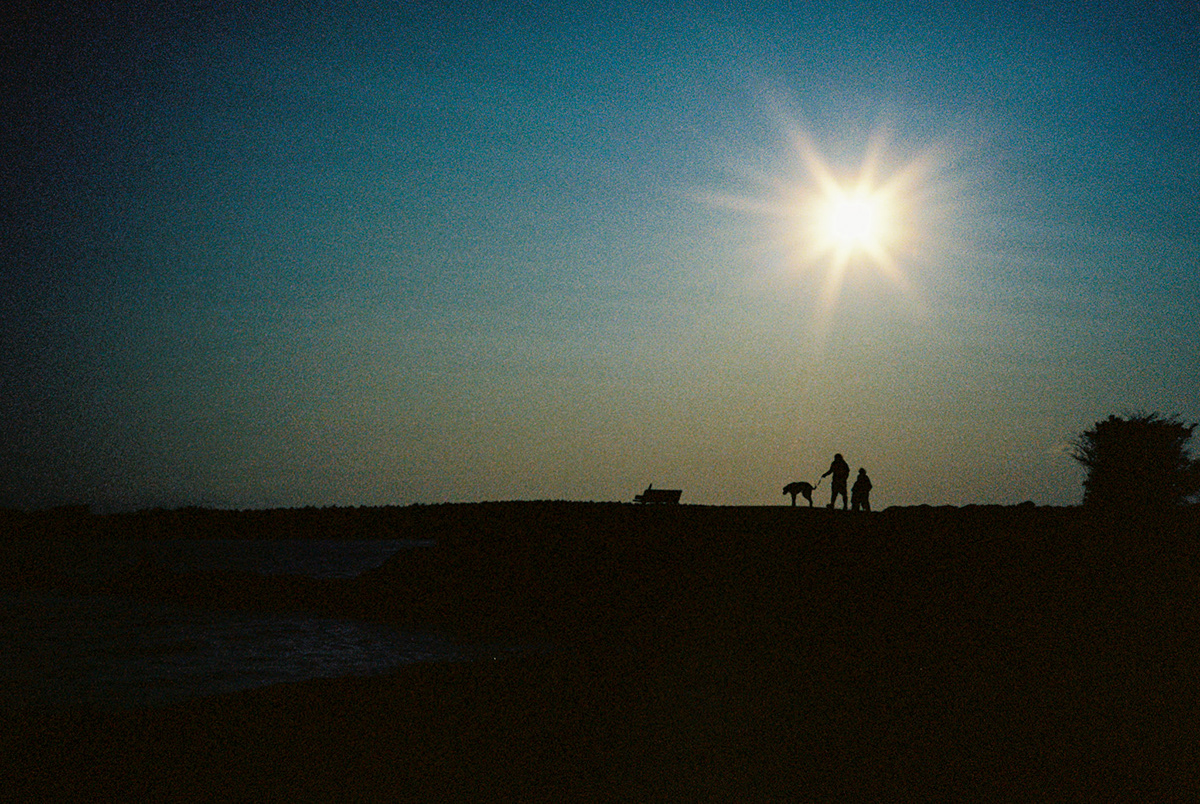 People silhouetted against a bright sun near the water